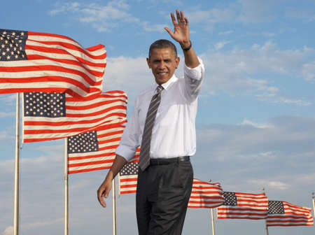 President Barack Obama waving against a backdrop of flags of the United States of Americaのeditorial素材