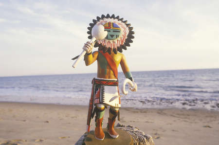 Hopi Kachina doll holding objects on beach with ocean in the backgroundのeditorial素材