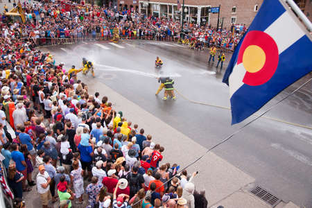Colorado flag hangs as men dressed in yellow firemen slickers and firehoses have annual Waterfight on July 4, Main Street, Ouray, CO, sponsored by Ouray Fire Departmentのeditorial素材