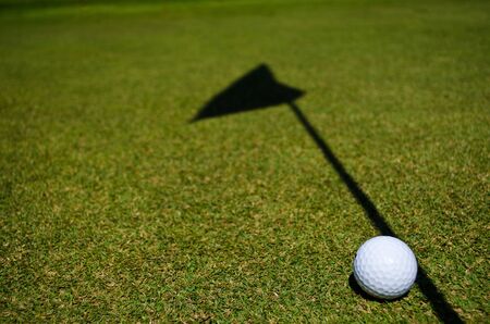 a golf ball and the shadow of the hole flagの写真素材