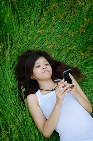 asian cute girl texting on meadow with happy faceの写真素材