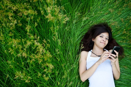 asian cute girl texting on meadow with happy faceの写真素材