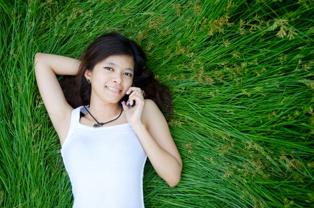 asian girl on phone lying on a meadowの写真素材