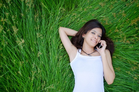 asian girl on phone lying on a meadowの写真素材