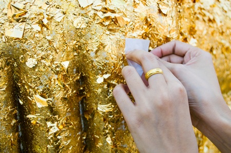 close up of buddhist's hand placing gold leaf on buddha statueの写真素材
