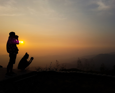 silhouette of couple taking photo of mountain peak against sunrise