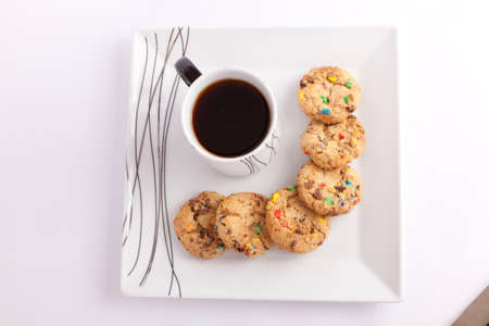 Cup of tea with cookies with colored chocolate on white dish