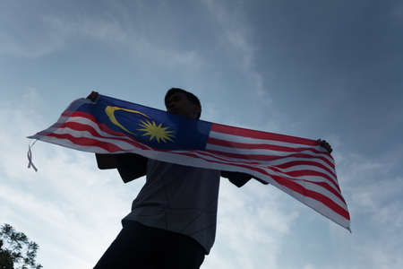 Independence Day concept. A happy and proud citizen holding Malaysian flag. sky background.