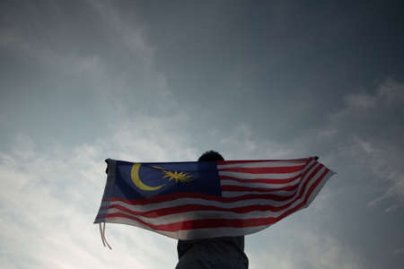 Independence Day concept. A happy and proud citizen holding Malaysian flag. sky background.