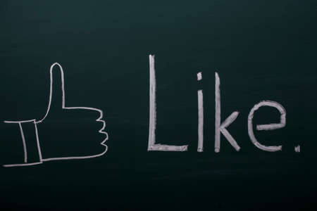 Thumbs up in front of a blackboard with the word Like written with white chalk on it.の写真素材