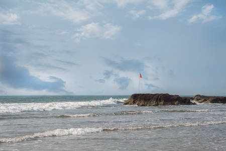 Sea and stones, Red flag fluttering in the wind.の写真素材