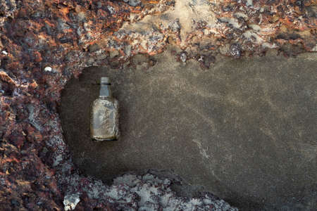 An empty glass bottle lies on the sand with reefsの写真素材