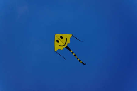 A yellow kite in a blue sky の写真素材
