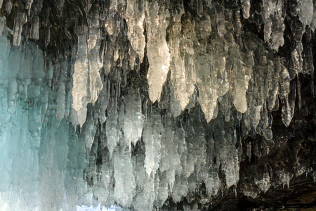 Icicles hanging from the ceiling of the stone cave and covering the entrance to the grotto Naples on lake Baikal. Photo toned.の写真素材