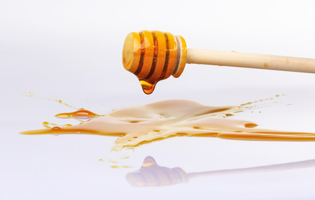 Honey dripping from wooden dipper for honey on white background. The reflection of the bowl for honey on the surface.の写真素材