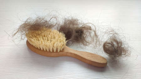 Close-up of a brush with lost hair on it on white wooden table. Concept of hair loss problem.の写真素材