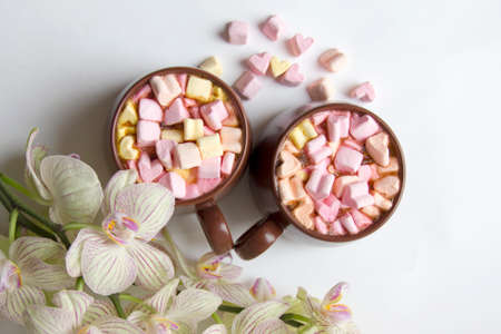 Top view of brown cups of hot cocoa with marshmallows in heart shape on white background. Romantic...
