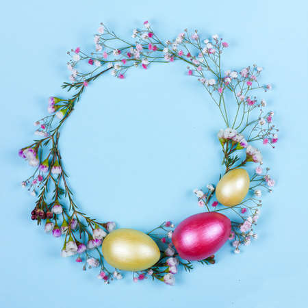 Easter wreath with spring flowers, green leaves and colored eggs on blue background. Creative Easter flat lay backdrop with space for text. Focus pickedの写真素材