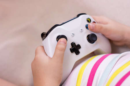 Closeup little girl hands hold a joystick. A child plays video games. Leisure time at home. view from the back.の写真素材