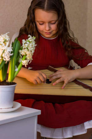 Cute little girl is playing the gusli - psaltery - at home. Traditional folk slavic string...