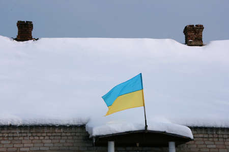 State flag of Ukraine on the porch in the background of snow-covered roof with chimneysの写真素材