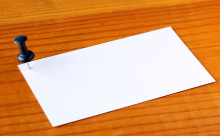 Close up of a note paper with push pin on wood background. Shallow depth of field. Focus on the pin. の写真素材