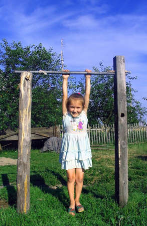 The little girl in a short dress costs on a grass and hands keeps for a crossbeam