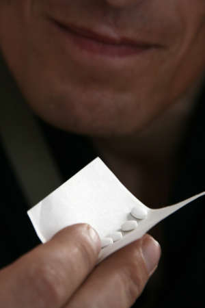 Hand holding a piece of paper with pills. Shallow depth of field. Focus on the first pill.