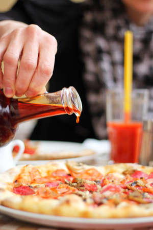 Female hand watering pizza sauce