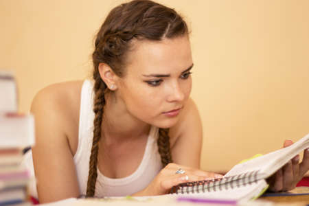Young girl doing homework assignment while relaxing in her bedroomの写真素材