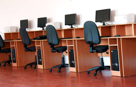 A number of tables with computers and chairs against the wall