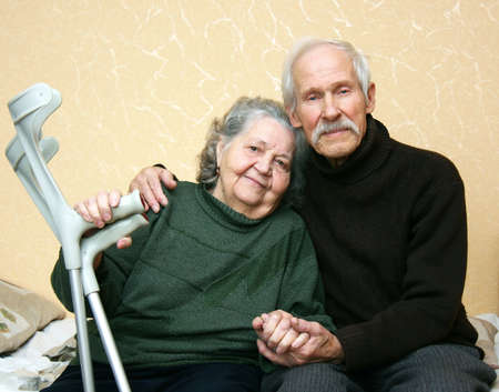Grandpa in a dark sweater gently embracing grandmother who keeps him at arm crutches の写真素材