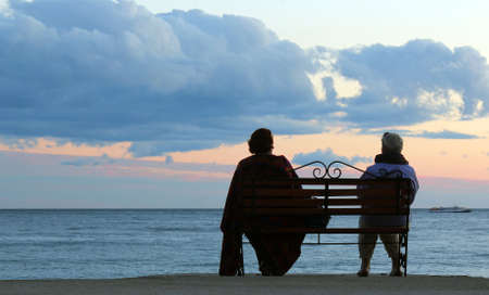 Elder couple couple sitting on a seaside bench enjoying the sunset over the sea の写真素材