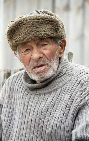 BYHIV, UKRAINE - JUNE 11 - An unidentified elderly man in winter hat in summer sitting at outdoor in...