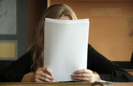 University student covering her face with papers and reading in classの写真素材
