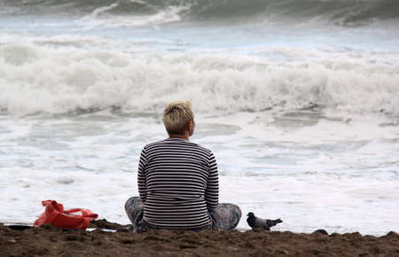 Woman sitting and relaxing on a sand by the sea, breathing fresh air on a beach and enjoying natureの写真素材