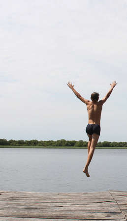 Young man jumping into the water with a wooden pier