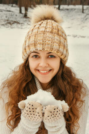 Girl with long hair and eyes of different colors in knitted hat playing with snow in park