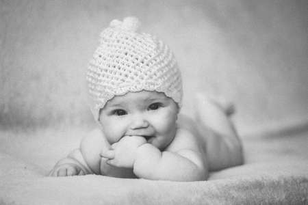Newborn baby girl in white hat on a bed. Black and white photo with grainy film effect.の写真素材