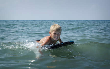 Boy has fun on the surfboard in transparency seaの写真素材