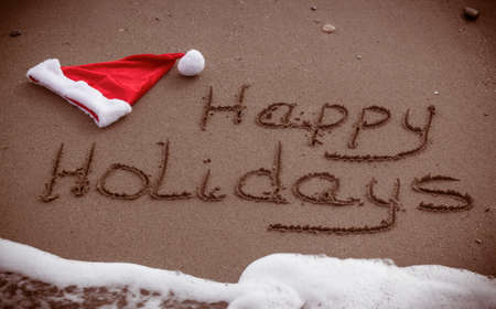 The words Happy Holidays written in wet sand with a Santa Hat on a beachの写真素材