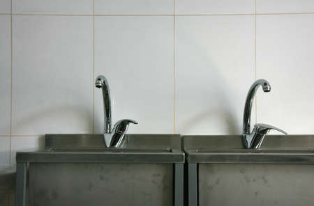 A photo of taps connected to two stainless steel basins on a beige work wallの写真素材
