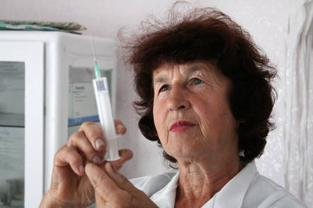 PLOSKE, UKRAINE - AUGUST 01 - Senior woman in white medical gown and a syringe at Ploske on August 01, 2008. In rural clinics doctors working in retirement age.のeditorial素材