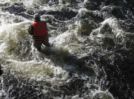 Man in the life vest standing in the water of the mountain river