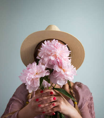 Funny portrait of blonde woman with hat close her face by bouquet. Shallow depth of field, focus on...