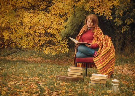 Woman sitting in the autumn park and read book with fall leaves on backgroundの写真素材