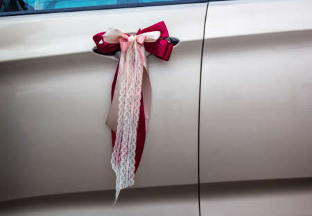 Red and pink decorative wedding ribbons on a door handle of a car