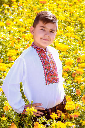 LUTSK, UKRAINE - 16 September 2016: Ukrainian schoolboy in embroidered shirt standing and posing among the marigoldsのeditorial素材