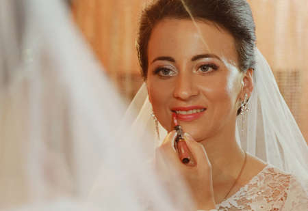 Beautiful brunette bride applying lipstick in the mirrorの写真素材