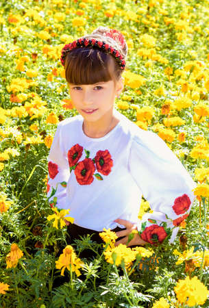 LUTSK, UKRAINE - 16 September 2016: Ukrainian schoolgirl in embroidered shirt standing and posing among the marigoldsのeditorial素材